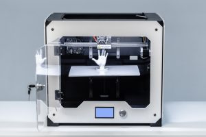 A 3D printer works to build a small hand model in a workshop during the morning hours.
